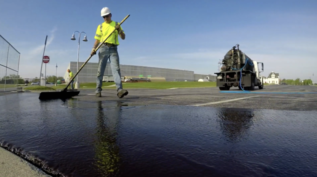 Site services crewman with a truck seal coating commercial parking lot