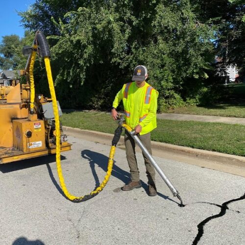 Site Services tech & equipment performing crack sealing in parking lot