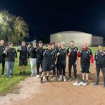 Site Services | Our local softball team photo. Site services employees together on a softball field at night, some holding equipment and gesturing thumbs up.