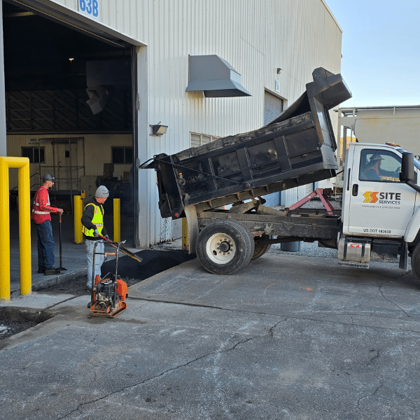 A dump truck unloads asphalt for patching.