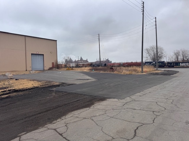 IMG_7690 Site Services | Overcast day at an industrial area with a beige warehouse, cracked pavement, railroad tracks, utility poles, and distant factory buildings.