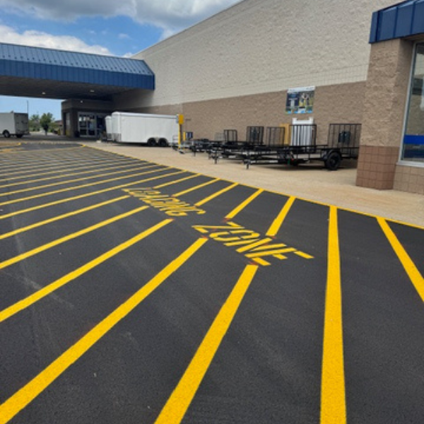 Lowes 1 Site Services | Freshly painted yellow lines from recent parking lot striping designate a loading zone in front of a commercial building with trailers and a covered entryway visible.