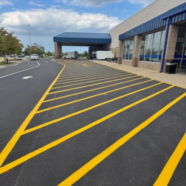 Lowes 2 Site Services | Freshly painted yellow diagonal lines from recent parking lot striping mark a no-parking zone outside a commercial building under a partly cloudy sky.