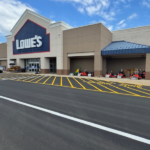 Site Services | Lowe's store exterior with lawn equipment displayed outside near the entrance, yellow-striped parking lot striping, and a marked “FIRE LANE” zone in front.