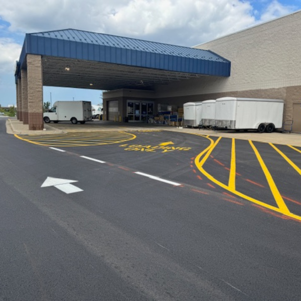 Lowes 4 Site Services | Covered loading zone outside a commercial building with a white truck, parked trailers, and fresh parking lot striping including yellow lines and an arrow on newly paved asphalt.